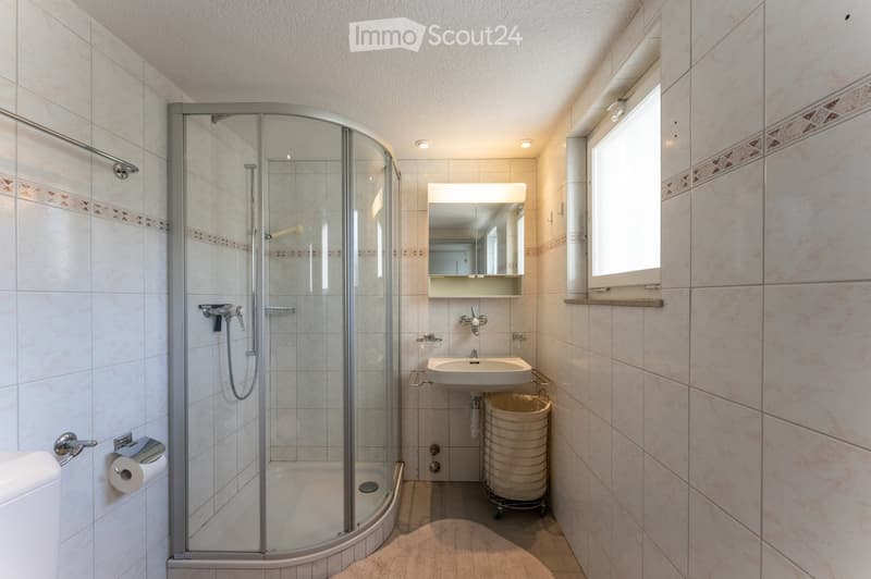 White tiled bathroom with a glass walk-in shower, white sink, mirror, and a toilet.