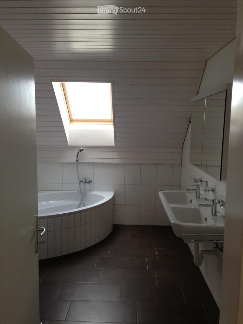 Modern bathroom with a large window, bathtub, double sink, and mirror.