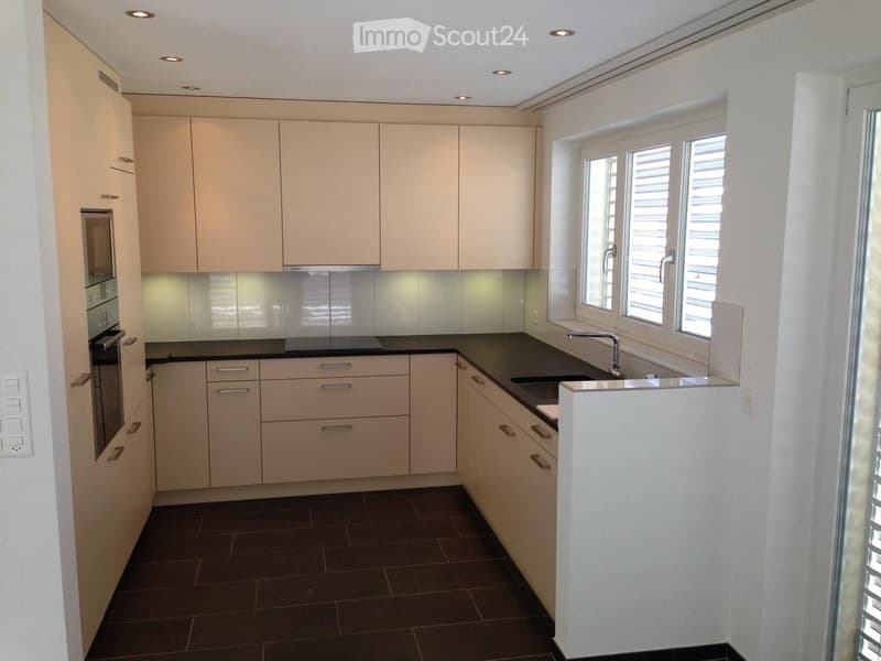 Modern kitchen with light-colored cabinets, dark countertops, and a sink with a faucet. Features include built-in oven and ample storage space.