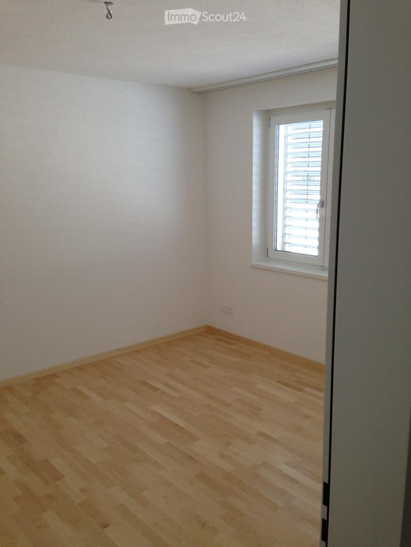 Empty room with light wooden flooring, white walls, and a single window with blinds.