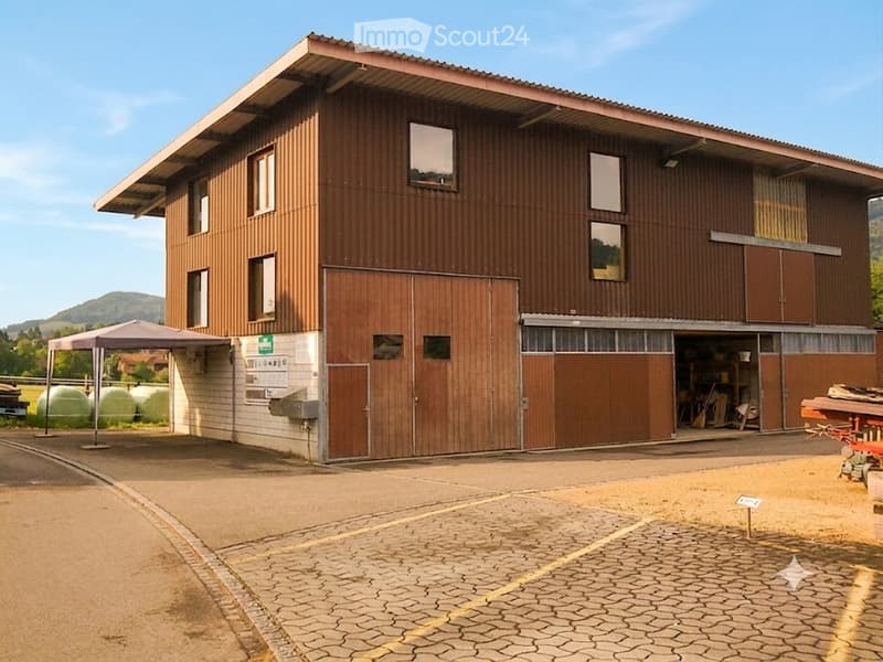 Two-story wooden building with large garage doors, multiple windows, and a covered outdoor area.