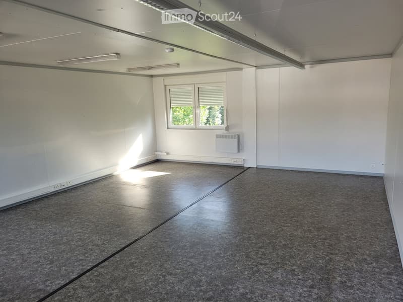 Empty room with white walls, grey tiled floor, and two windows with blinds. No furniture or equipment present.