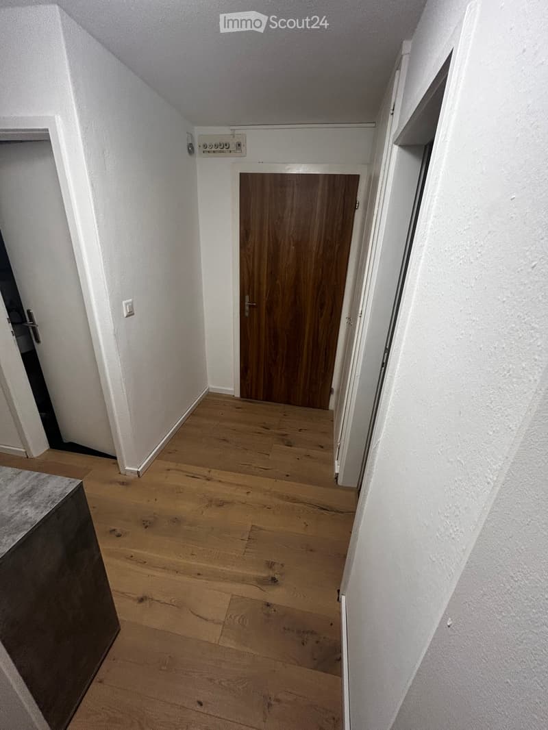 Empty hallway with wooden flooring, white walls, and a closed wooden door at the end.