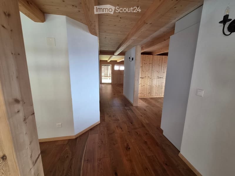 Empty wooden hallway with light-colored walls, wooden floor, and exposed wooden beams on the ceiling. Features a small window at the end and built-in wooden cabinets on one side.