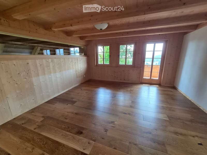 Empty room with wooden floors, wooden walls, and large windows, featuring a built-in wooden bench along one wall.