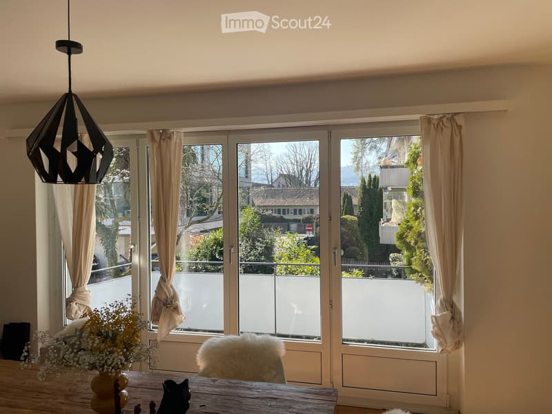 dining room with large windows, wooden table, white chair, flowers, balcony