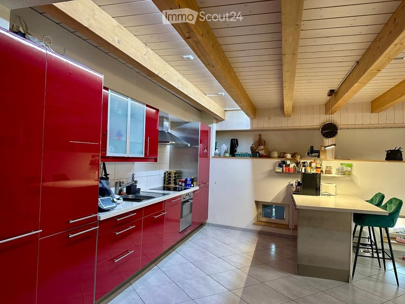 Modern kitchen with red cabinets, stainless steel appliances, island with bar stools, and exposed wooden beams on the ceiling.