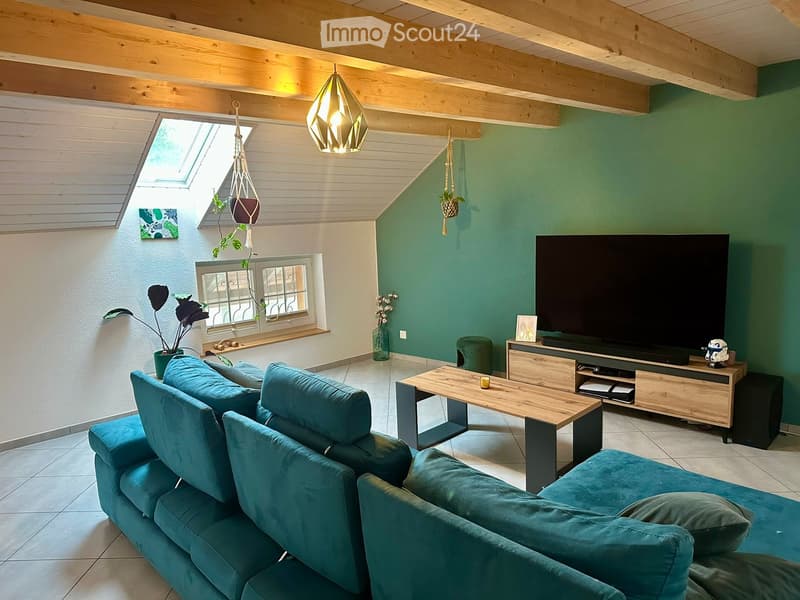 Modern living room with teal sofa, wooden coffee table, flat-screen TV on wooden stand, hanging plants, and decorative items.