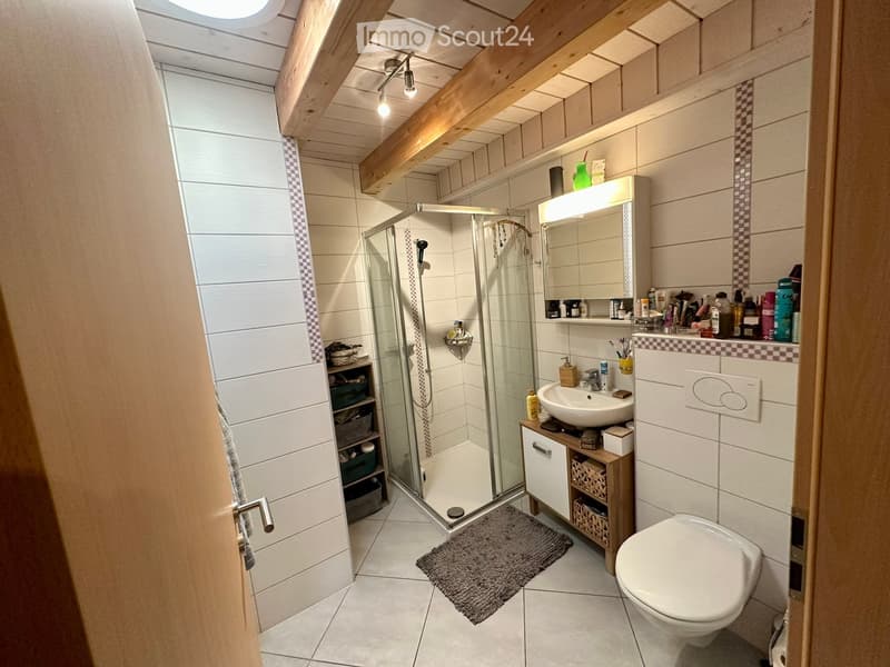 Modern bathroom with white tiles, a glass-enclosed shower, a toilet, a sink with a mirror, and a wooden cabinet with shelves.