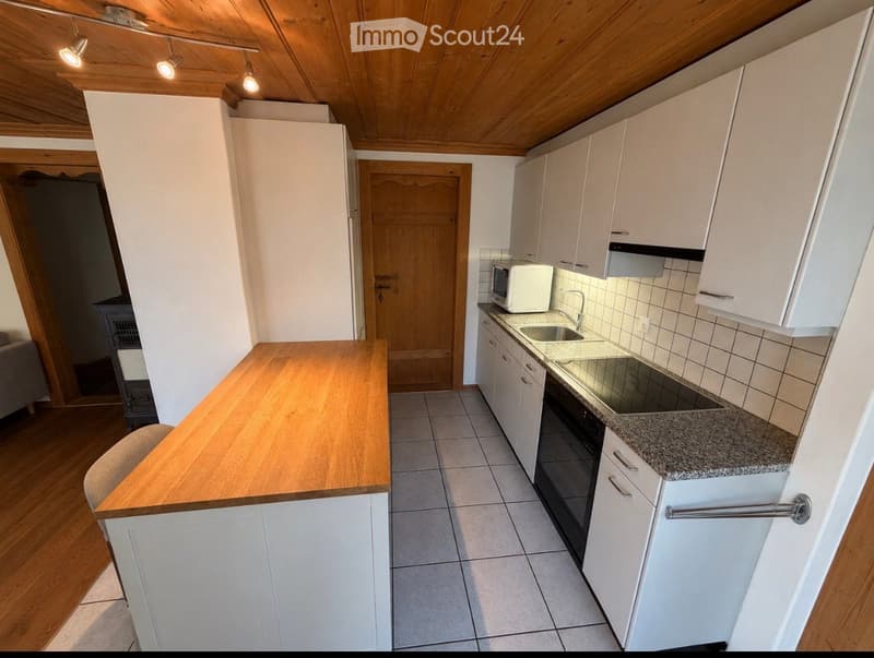Modern kitchen with white cabinets, granite countertop, stainless steel sink, microwave, and built-in oven. Wooden island with seating area.