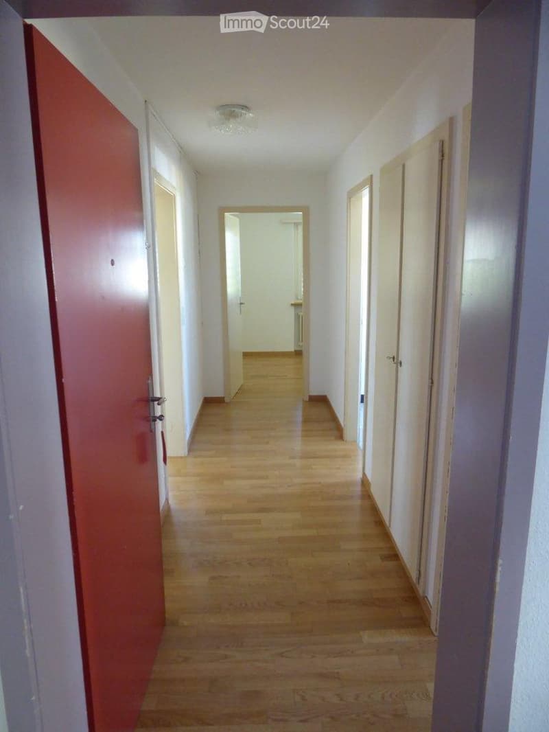 Empty hallway with wooden flooring, white walls, and several doors leading to other rooms.