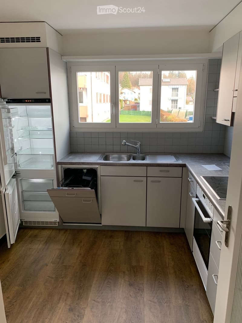 Modern kitchen with light wood flooring, white cabinets, stainless steel appliances including a refrigerator, dishwasher, and oven, and a sink with a faucet.