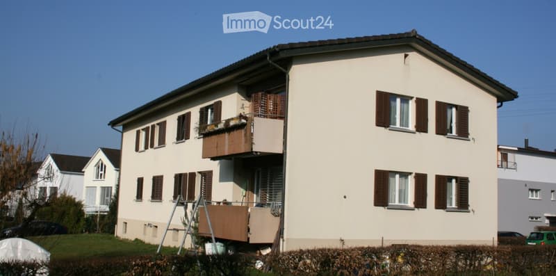 White 2 story building, brown windows with shutters, balcony on 2nd floor, green car parked in front
