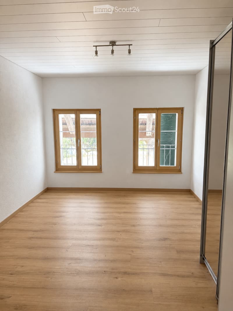 Empty room with light wooden flooring, white walls, and two wooden-framed windows with glass panels.