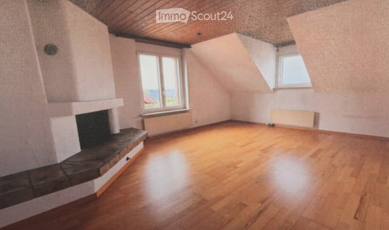 Empty room with wooden flooring, white walls, fireplace, and windows allowing natural light.
