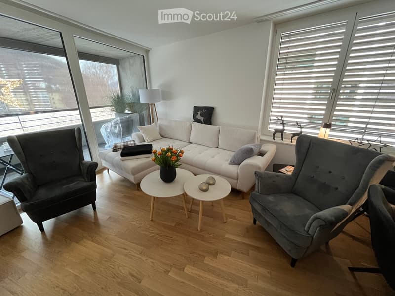 Modern living room with light-colored sofa, two armchairs, small round tables, a vase with flowers, and decorative items on the windowsill.