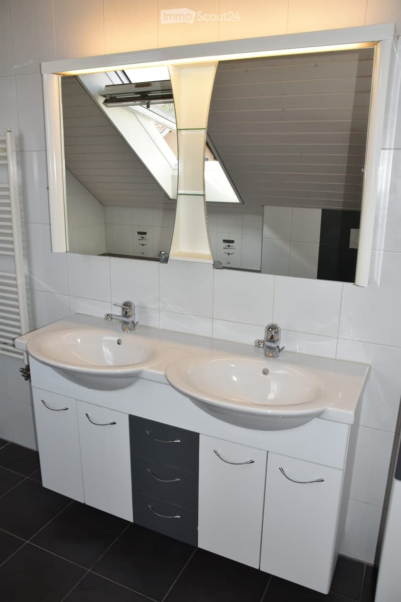 Modern bathroom with double sink vanity, white cabinets, black tiled floor, and large mirrored cabinet with built-in lighting.