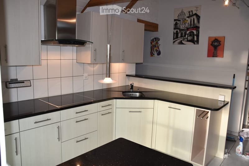 Modern kitchen with white cabinets, black countertops, stainless steel sink, stove, and range hood. Features a pendant light and several wall-mounted artworks.