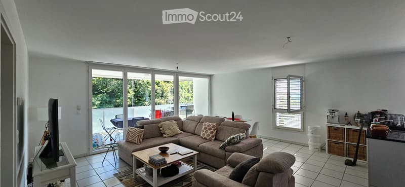 Modern living room with large sliding glass doors leading to a balcony, a sectional sofa with throw pillows, a coffee table, and a TV stand.