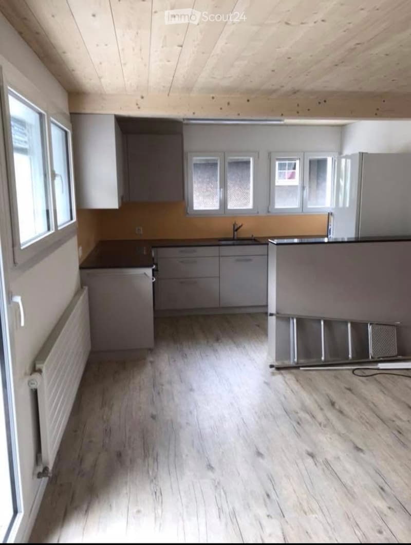 Empty kitchen with light wood flooring, grey cabinets, and a stainless steel sink. The space is unfurnished and ready for setup.