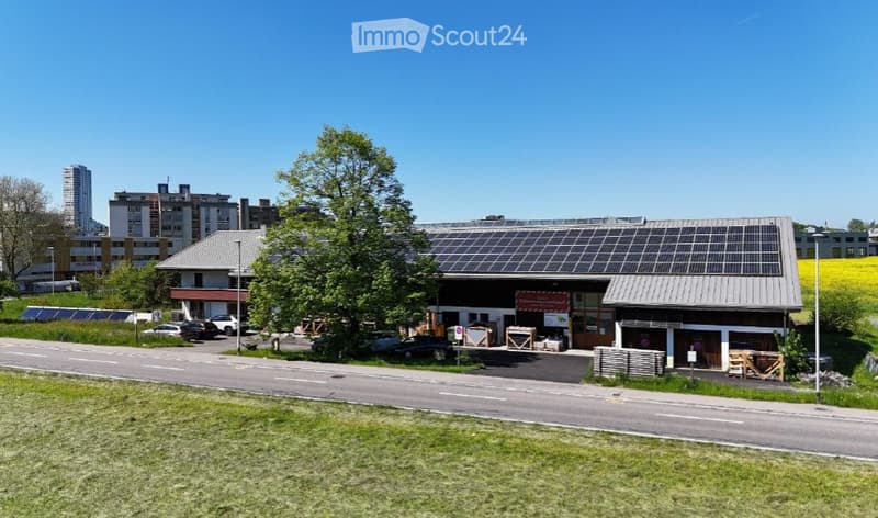 Modern building with solar panels on the roof, surrounded by trees and parked cars.