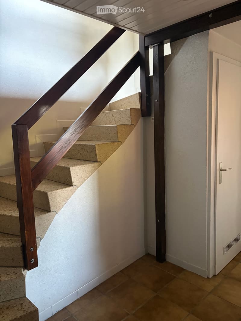 Modern staircase with wooden handrail and beige tiled steps, leading to a closed door on the right side.