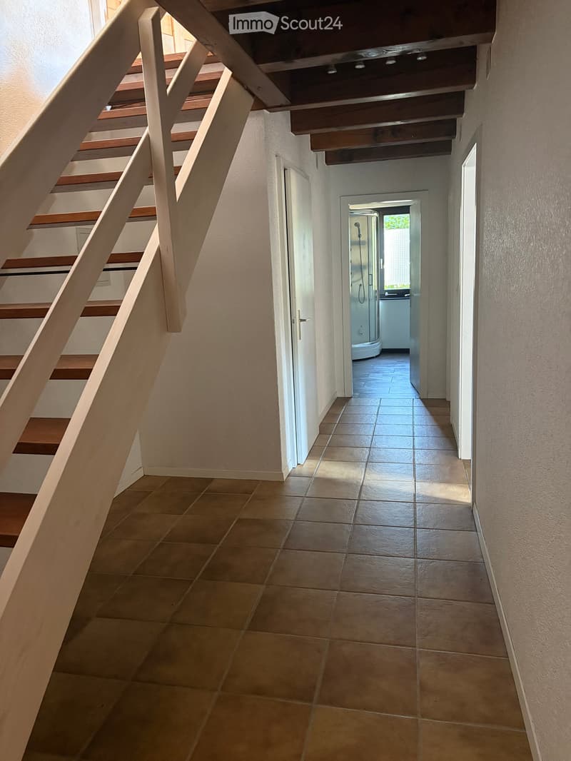 Hallway with tiled floor, wooden staircase, and open doorway leading to a bathroom.