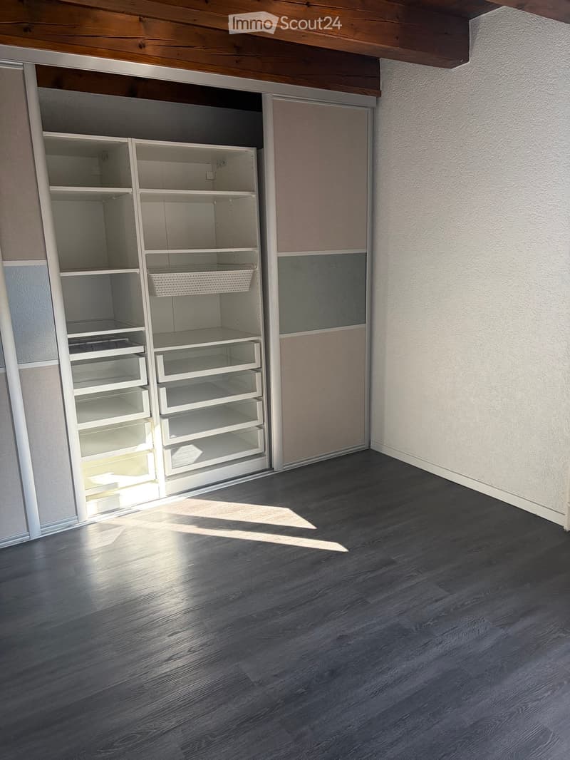 Empty room with dark wooden flooring, white walls, and built-in white shelving unit with multiple compartments and drawers.