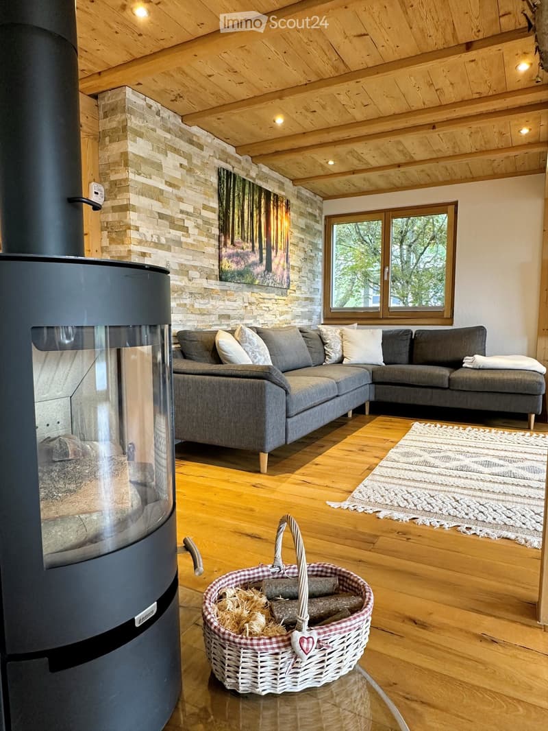 Cozy living room with wooden ceiling, exposed wooden floor, grey sectional sofa, fireplace, and a basket of firewood.
