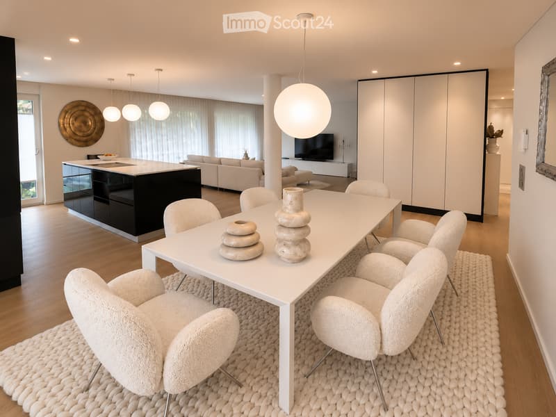 Modern, open-plan living and dining area with a white dining table, six white chairs, a black kitchen island, a light grey sofa, a flat-screen TV, decorative vases, and pendant lights.