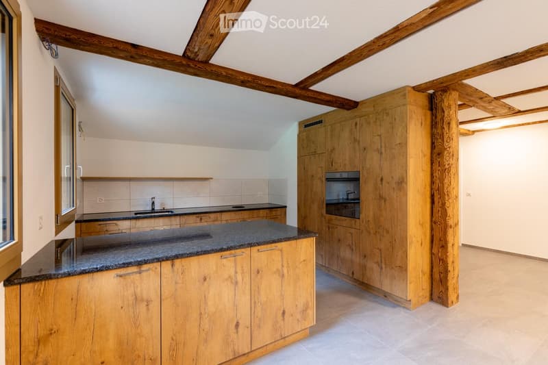 Modern kitchen with wooden cabinets, granite countertop, sink, and built-in oven. Exposed wooden beams on the ceiling.