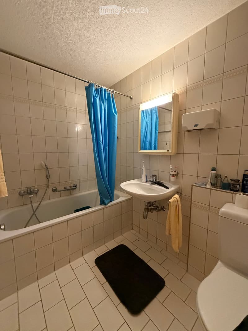 Bathroom with a bathtub, sink, mirror, toilet, towel, and a black bathroom mat on the floor.