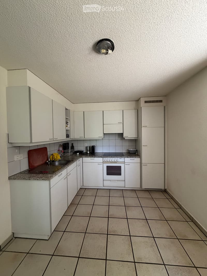 A modern kitchen with white cabinets, a tiled floor, and a granite countertop. The kitchen features an oven, sink, and various small appliances.