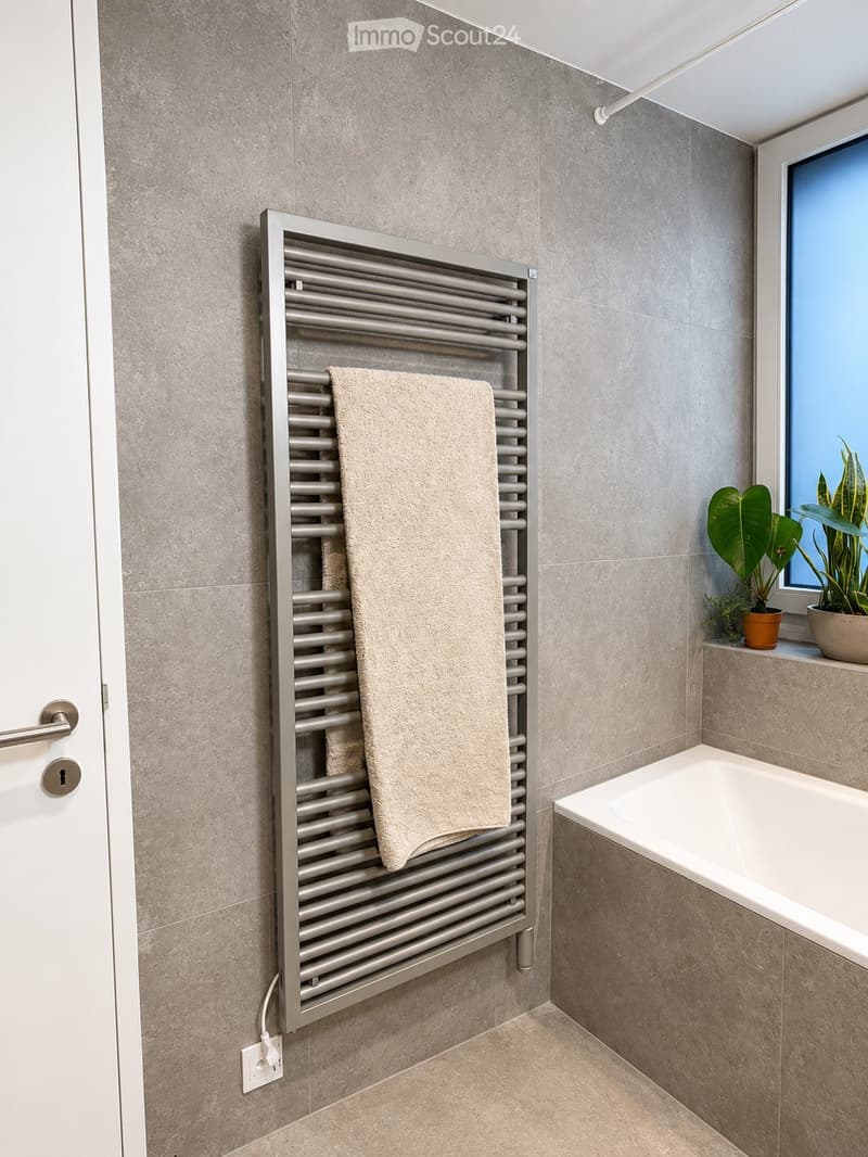 Modern bathroom with a bathtub, a towel on a radiator, and potted plants on the windowsill.
