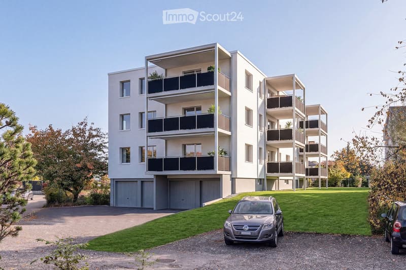 Modern multi-story apartment building with balconies, garage, and parking area.