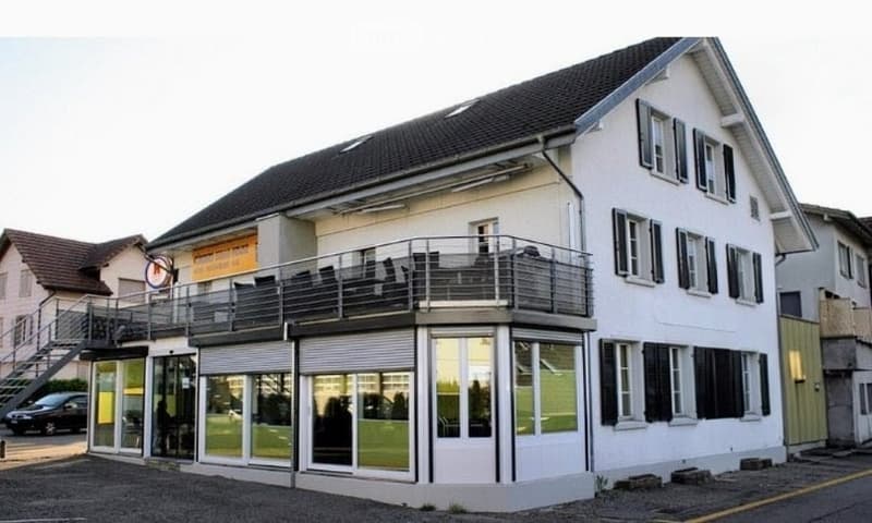 Two-story building with a balcony on the first floor, large windows, and a covered entrance area.