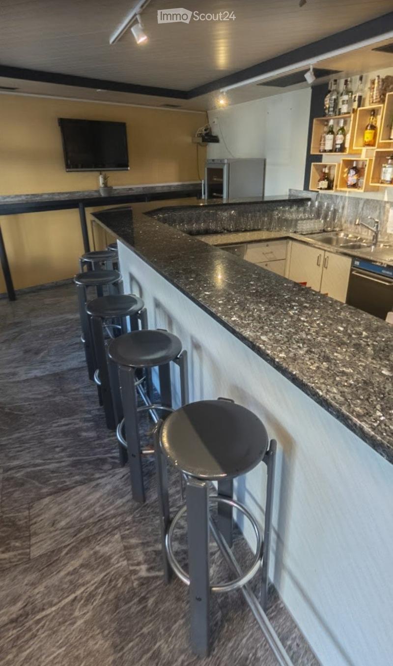 Bar area with granite countertop, bar stools, sink, refrigerator, and shelves with bottles.