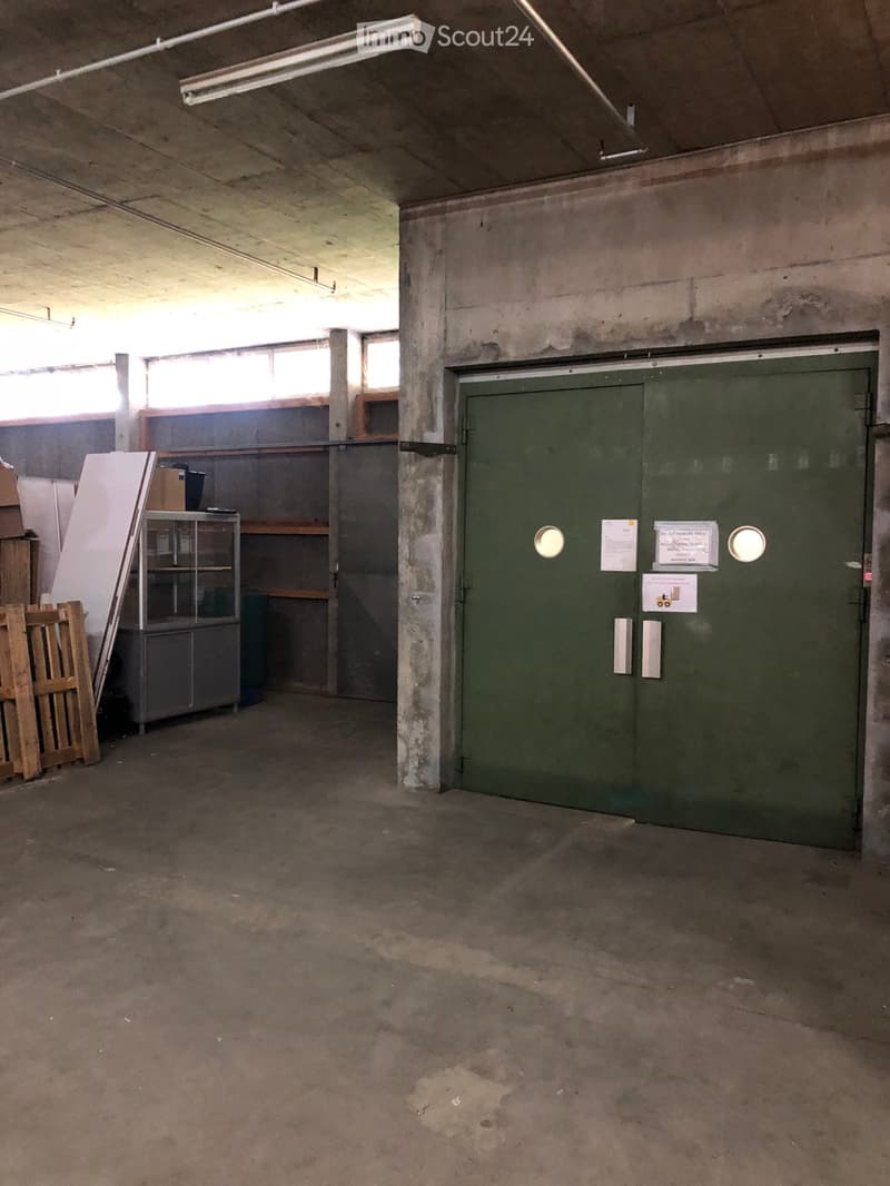 Empty garage with concrete floor, large green roll-up door, metal shelving unit, and some storage items in the corner.