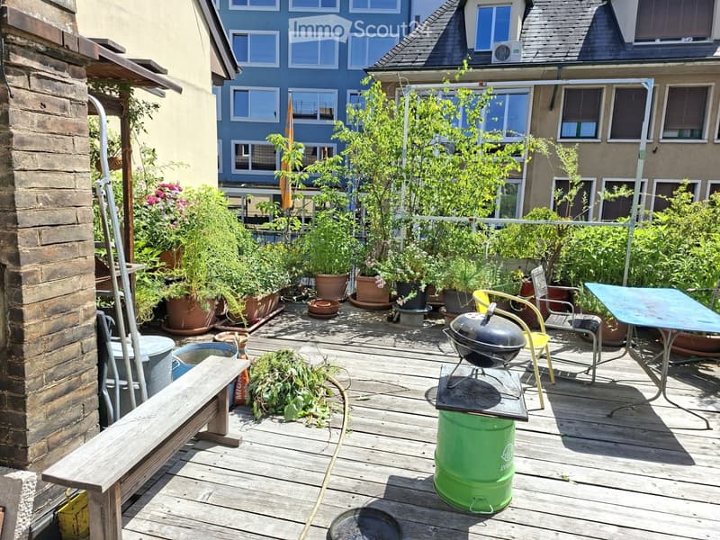 Wooden deck with a bench, table, chairs, grill, and several potted plants.