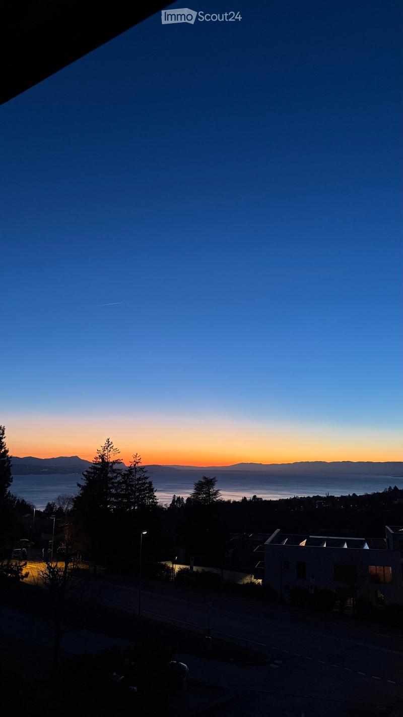 Balcony view at sunset over a body of water with distant mountains, trees, and a road below.