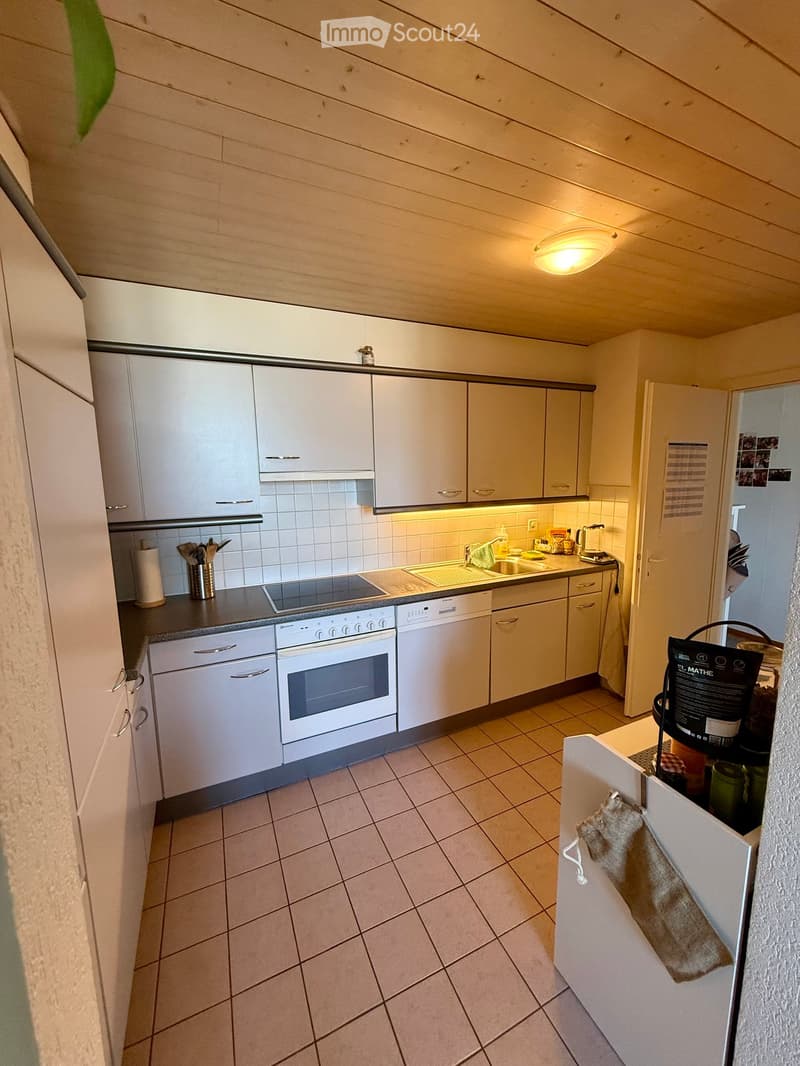 Modern kitchen with white cabinets, stainless steel appliances, tiled floor, and warm lighting.