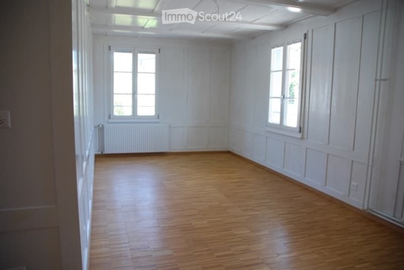 Empty room with wooden flooring, white walls, and two windows allowing natural light. No furniture or equipment present.
