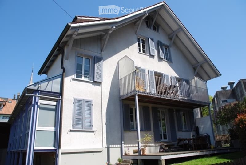 Two-story house with white siding, blue shutters, and a balcony with outdoor furniture.
