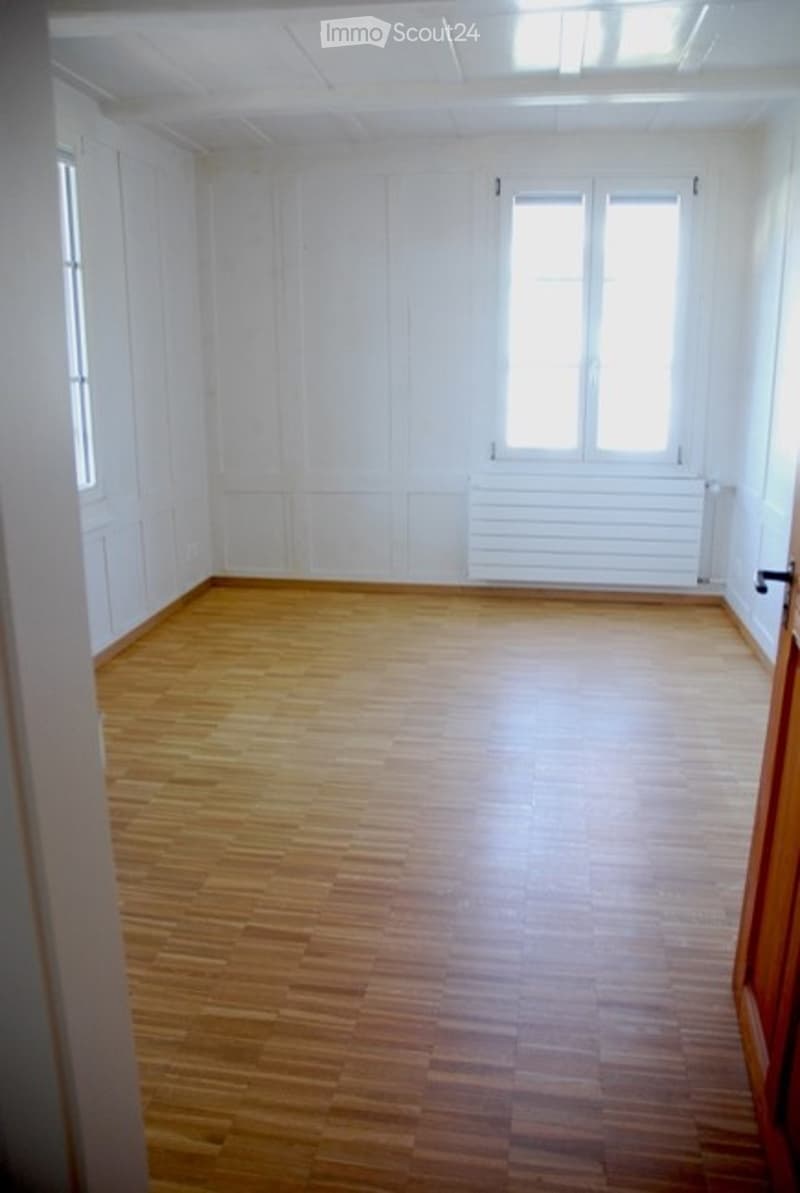 Empty room with wooden flooring, white walls, and large windows. No furniture or equipment present.