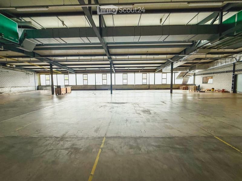 Large, empty industrial-style room with concrete floors, exposed metal beams, and large windows allowing natural light. Minimal furnishings, including a few crates and storage boxes.