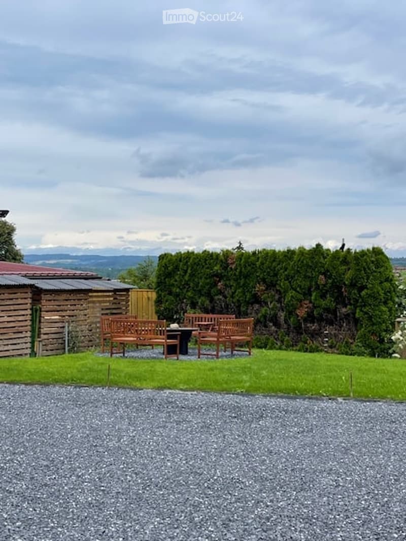 well-maintained garden with grassy lawn, wooden bench seating, gravel driveway, shrubs, wooden shed, mountain view in the distance