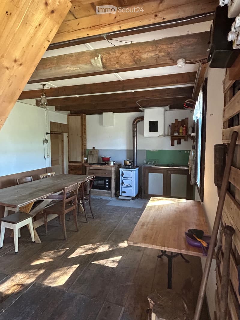 A rustic kitchen with wooden beams, a wooden dining table, chairs, a stove, and cabinets.
