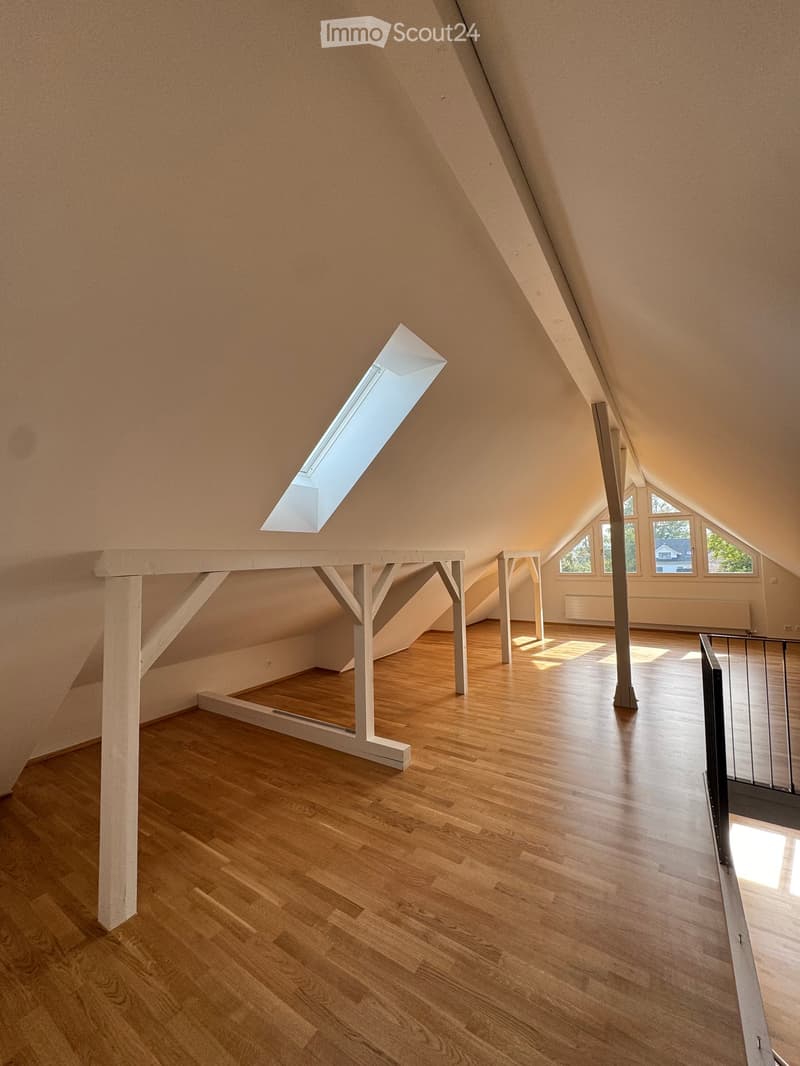 Empty attic space with wooden flooring, slanted ceilings, skylight window, and built-in wooden platform structure.