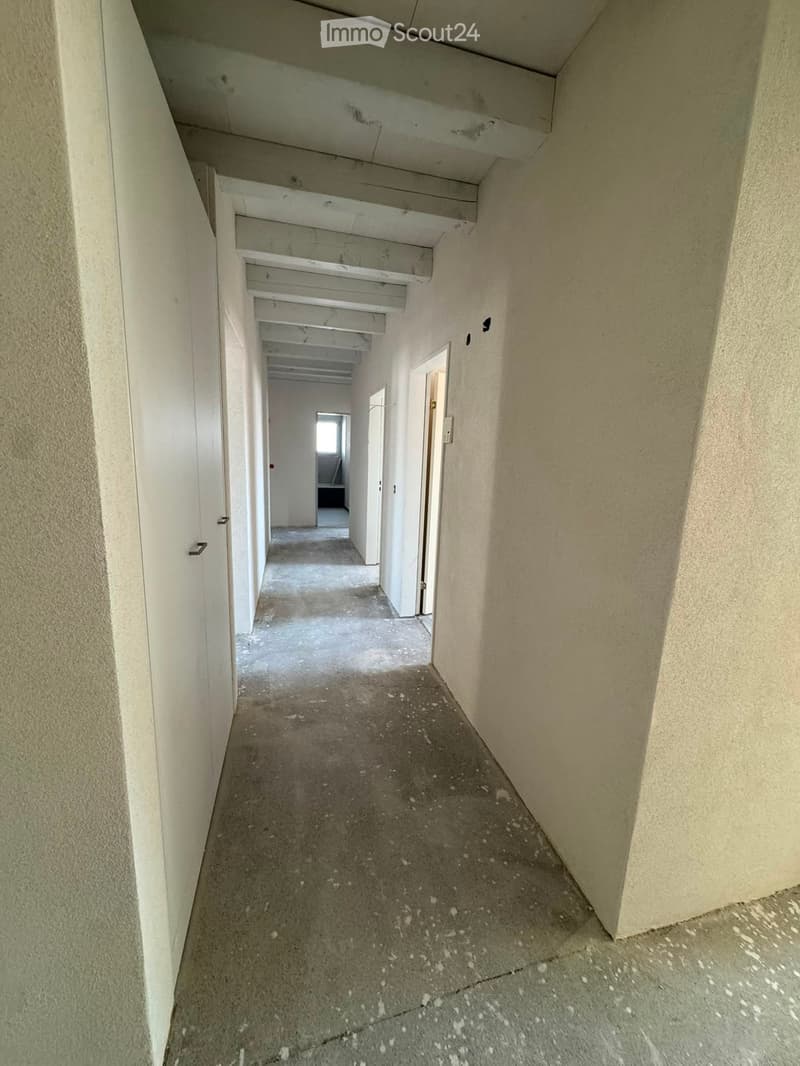 Empty hallway with concrete floors, white walls, and multiple doors leading to other rooms.