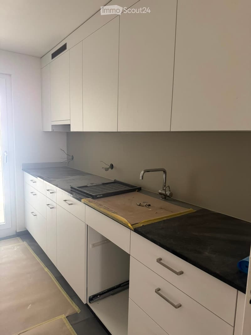 Modern kitchen with white cabinets, black countertop, and a sink with a faucet. The countertop has a protective sheet and some tools.
